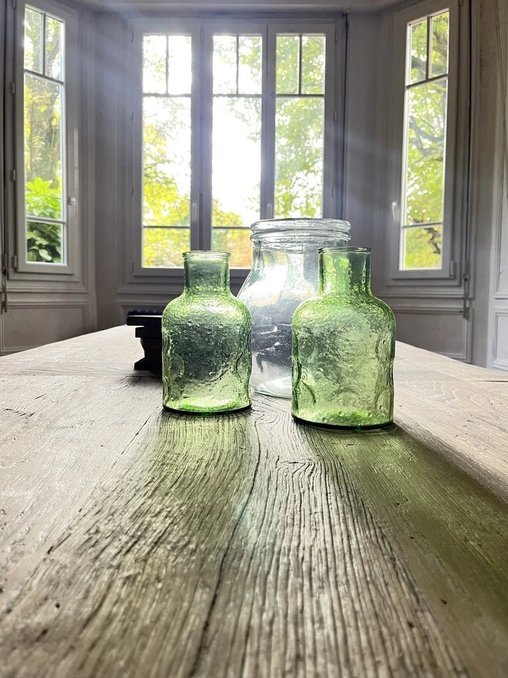 Détail du plateau en chêne massif ancien de la table Founder avec bouteilles décoratives.