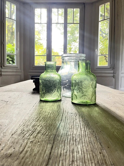 Détail du plateau en chêne massif ancien de la table Founder avec bouteilles décoratives.