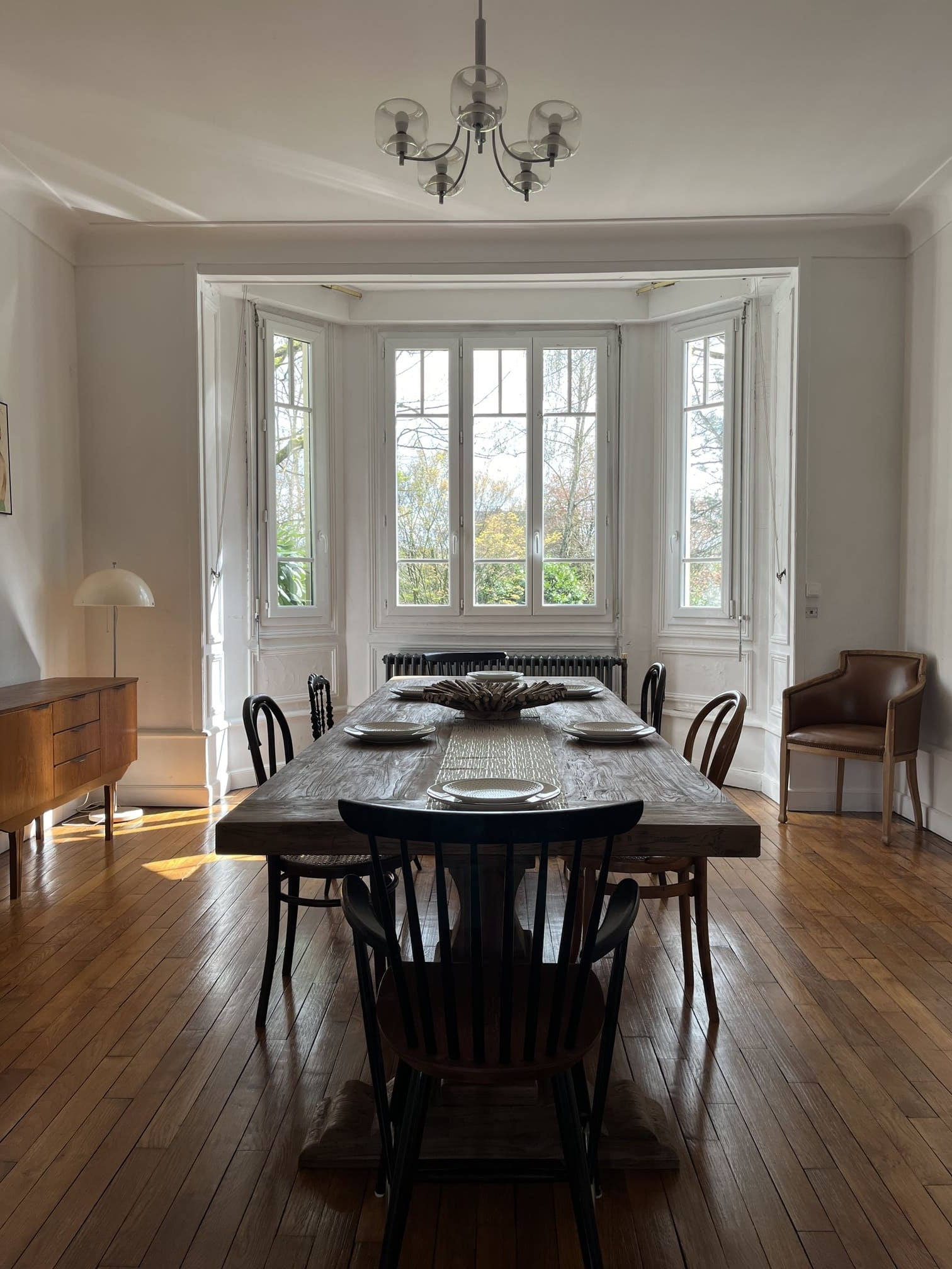 Table Monastère Spirito en bois massif face aux grandes fenêtres, ambiance lumineuse et chaleureuse.