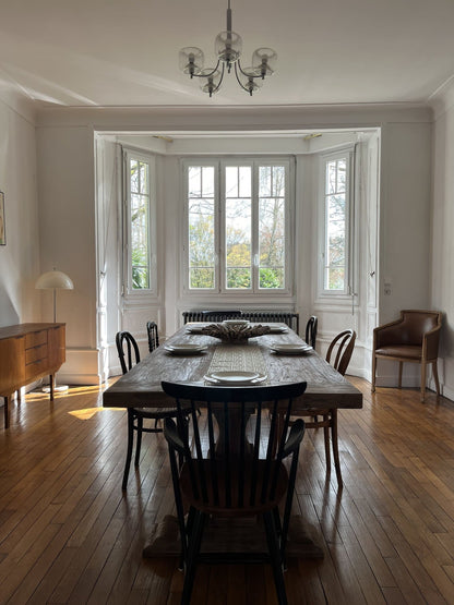 Table Monastère Spirito en bois massif face aux grandes fenêtres, ambiance lumineuse et chaleureuse.